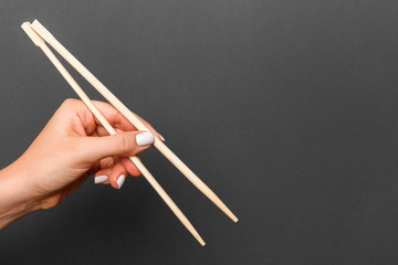 Wall Mural - Creative image of wooden chopsticks in female hand on black background. Japanese and chinese food with copy space