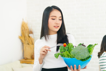 asian beauty woman stand holding fork with tomato and holding salad bowl in house.