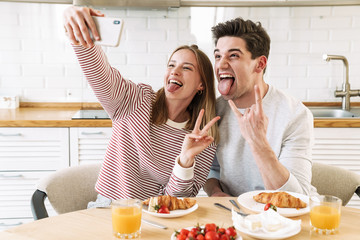 Wall Mural - Portrait of couple taking selfie on smartphone while having breakfast