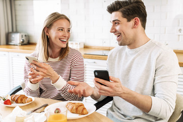 Wall Mural - Portrait of couple using smartphones and talking while having breakfast