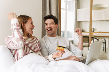 Sticker - Portrait of excited couple holding credit card while using laptop