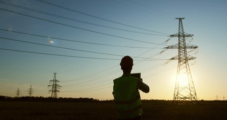 Wall Mural - the power engineer conducts a power line state inspection using a tablet, sunset background.