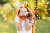 Fototapeta Dmuchawce - Little girl blowing gold confetti with her hand.