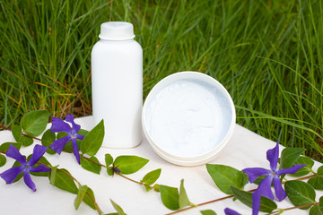 Wall Mural - body cosmetics with violet flowers on a background of green grass. skin care, beauty, spa