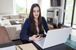 © zphoto83 - Young woman working from home, holding mobile phone and using laptop at the desk. Online meeting concept.