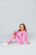© Julie Boro - girl in a pink tracksuit and sneakers sits on a light gray background