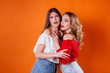 © Andrii - Two young and beautiful girls shows emotions and smiles in the Studio on an orange background. Girls for advertising