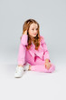 © Julie Boro - cute girl in a pink tracksuit and sneakers sits on a light gray background