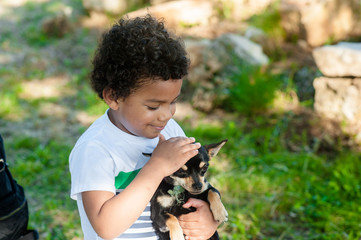 African young boy holding his little dog in nature.