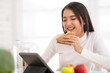 © Success Media - Young Asian woman working with tablet at home and eating sandwich  salad fruits at home