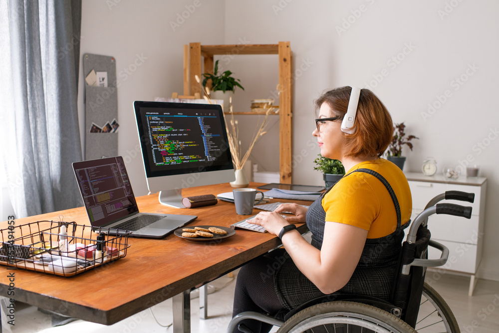 Smart disabled coder sitting in wheelchair and using computers while working from home - obrazy, fototapety, plakaty 