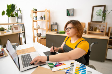 Content creative young disabled woman sitting in wheelchair and using tablet while working on graphic design