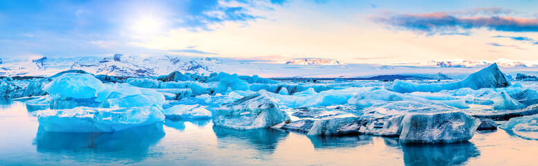 icebergs float on jokulsarlon glacier lagoon, with background mountain peaks lit by sunrise, in icel