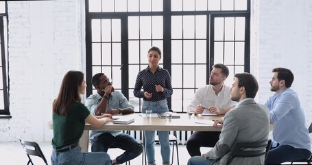 Wall Mural - Attractive female indian team leader motivating diverse coworkers at brainstorming meeting in office. Focused young mixed race colleagues listening to supervisor, sharing project ideas at workplace.