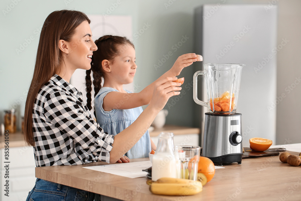Mother and little daughter making healthy smoothie in kitchen