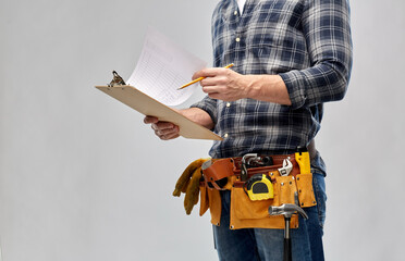 repair, construction and building - male worker or builder with clipboard, pencil and working tools on belt over grey background