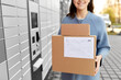© Syda Productions - mail delivery and post service concept - close up of happy smiling woman with boxes at outdoor automated parcel machine