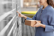 © Syda Productions - mail delivery and post service concept - close up of happy smiling woman with box at outdoor automated parcel machine choosing operation on touch screen