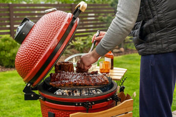 Red Ceramic Barbecue Grill. The man supervises the Grilling, Smoking, Baking, BBQ and Roasting process.  Post-quarantine Picnic in  homes terrace.