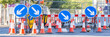 Four Round Blue Road Signs Each Containing a White Arrow Indicating a Mandatory Directional Instruction to Motorists.  Several Traffic cones in Front.  Panoramic Crop