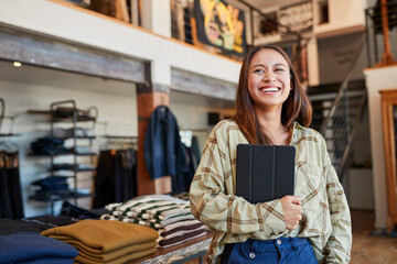 Portrait Of Female Owner Of Fashion Store Using Digital Tablet To Check Stock In Clothing Store