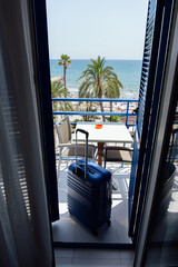 Suitcase on balcony with palm trees and seascape at background in Catalonia, Spain