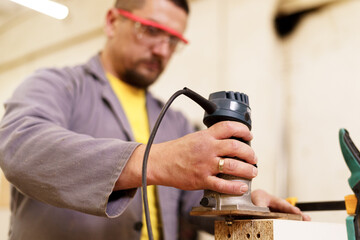 Wall Mural - Carpenter sanding a wood with sander wearing safety goggles in his workshop. Man loves his job.