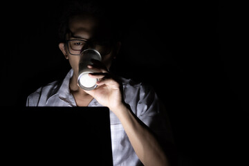 Wall Mural - Low light view and copy space. A man drinks milk while using a laptop. He works online at home late at night.