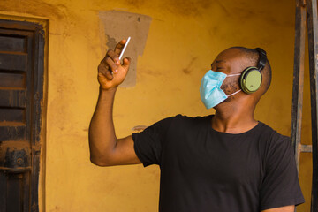 Wall Mural - young black man wearing a nose mask, listening to songs on his phone with a wireless headphone