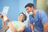 Fototapeta  - Dentist shows the patient the results of treatment with a mirror, examinating teeth with dental equipment in dental office. Young handsome male doctor in medical facial mask and smiling happy woman.