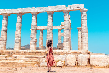 Wall Mural - A young girl walks around ancient temple of Poseidon on the Cape Sounion during a long-awaited summer vacation in Greece