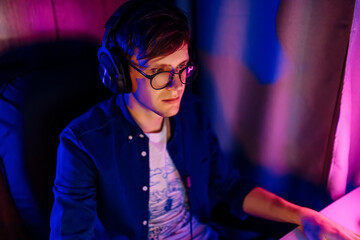 A happy gamer with glasses and a headset plays computer games at home. Technology, games, entertainment