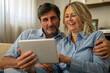 © Kitreel - A happy mature couple is using a tablet for family entertainment while sitting on a sofa in living room at home.