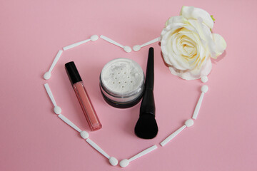 Wall Mural - powder, lipstick and black powder brush in a heart of white shadow applicators and a rose on a pink background