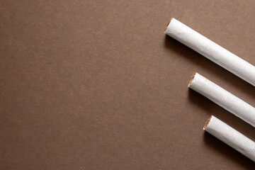 Three cigarettes lined up on a brown background. Area left for copyspace