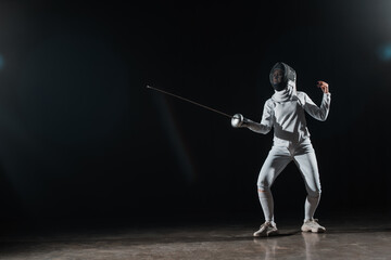 Fencer training with rapier under spotlight on black background