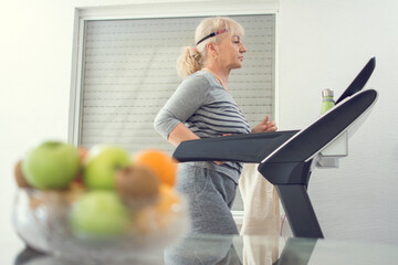 Active senior woman in sportswear jogging on treadmill at home. Home workout, active seniors, stay at home concept.