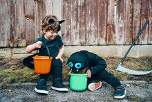 Two Children Dressed For Halloween Sitting At The Side Of The Road Looking Into Their Buckets Of Sweets.