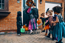 A Group Of Children Dressed Up For Halloween At A Front Door With Buckets Trick Or Treating.