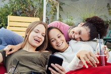 Three Women Lounging Together, Laughing And Looking At A Mobile Phone.