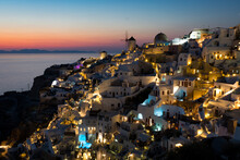 Sunset In Oia Village On Santorini, Greece. Famous Santorini Sunset Capture. Windmills And Churches In The Background. 
Blue Dome Church.