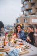 © Maskot - Happy female sitting with friends while talking on building terrace during sunset