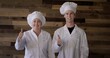 © vesperstock - MS Mature woman and young man in chef hats and white coats with 'I voted' stickers and giving thumbs up. Neutral wood plank background