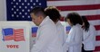 © vesperstock - MS Group of four scientists or doctors of various demographics, all in white lab coats, voting at booths in polling station during US election