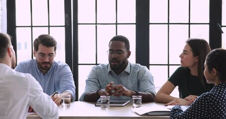 Wall Mural - Head shot confident skilled young african american boss executive in eyeglasses talking to multiracial coworkers at business meeting. Focused mixed race employees listening to biracial team leader.