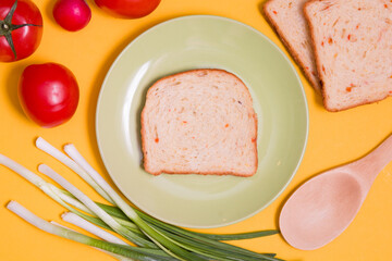 breakfast concept, a piece of bread on a green plate and vegetables on a yellow background, top view, mock up, bread, vegetables, green onions, tomatoes, radishes, vegan breakfast