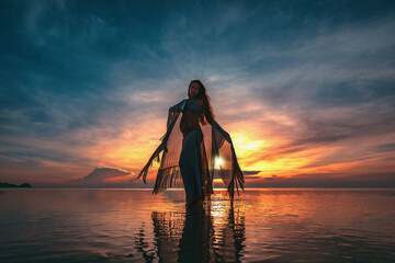 silhouette of young fashionable woman standing in water on the beach at sunset