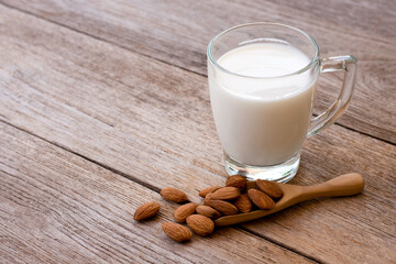 Poster - Glass of Almond milk and almond seeds in wooden scoop isolated on wood table background. Healthy drinks concept.