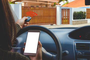 Young asian woman in car hand holding mobile smart phone with blank white screen and using remote control to open or close the auto gate when driving. Home security and electric door,wireless concept.