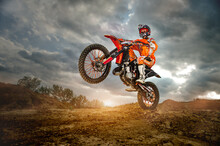 Side View Of The Professional Motorcycle Rider Driving On The Mountains And Further Down The Off-Road Track. It's Sunset.